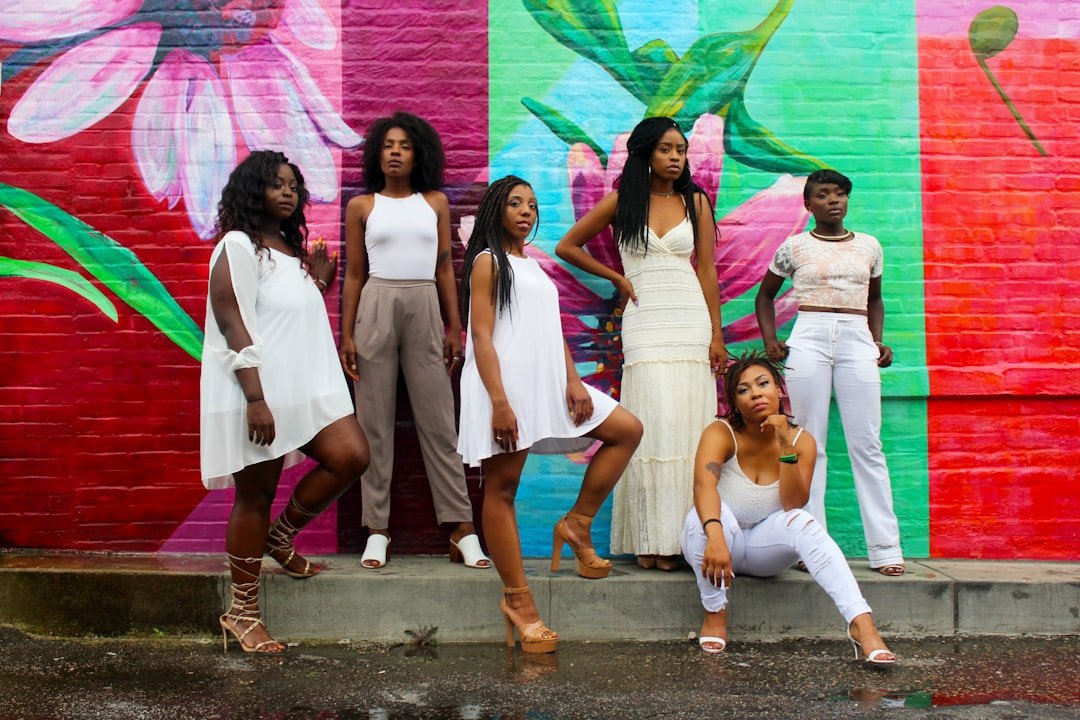 Six women wearing white pants posing together, smiling and showing unity and empowerment.